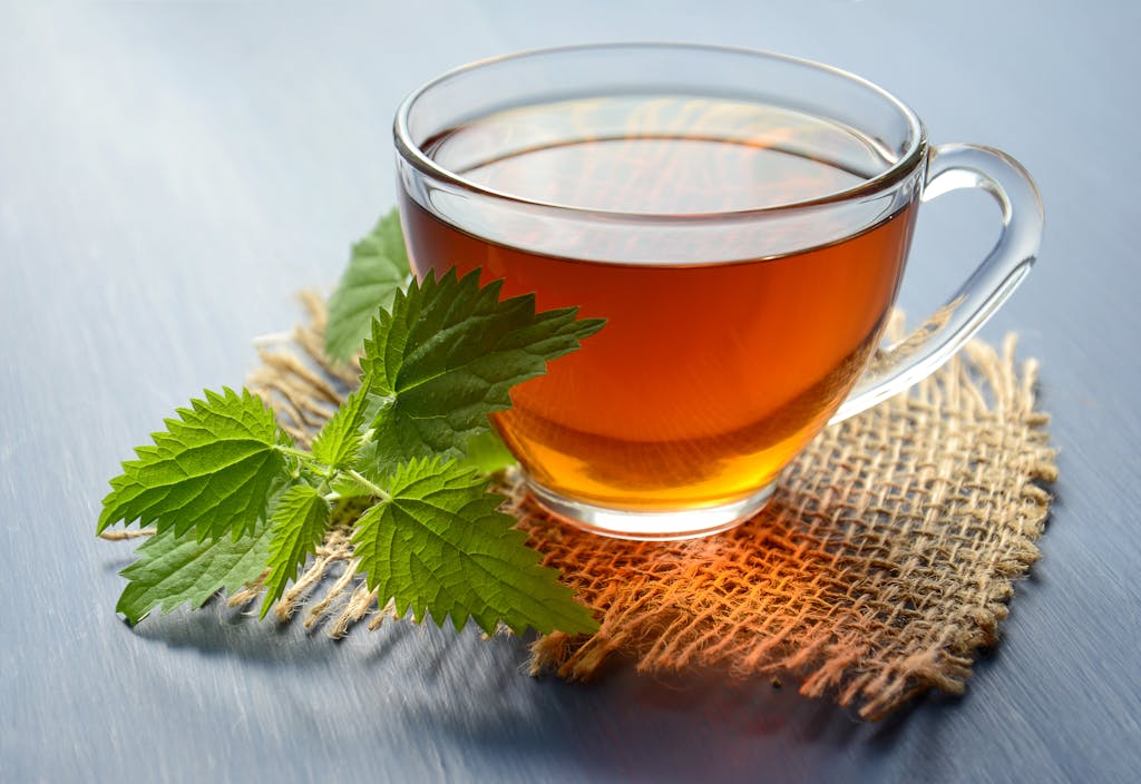 A close-up of herbal tea in a glass cup with fresh mint leaves on a table.